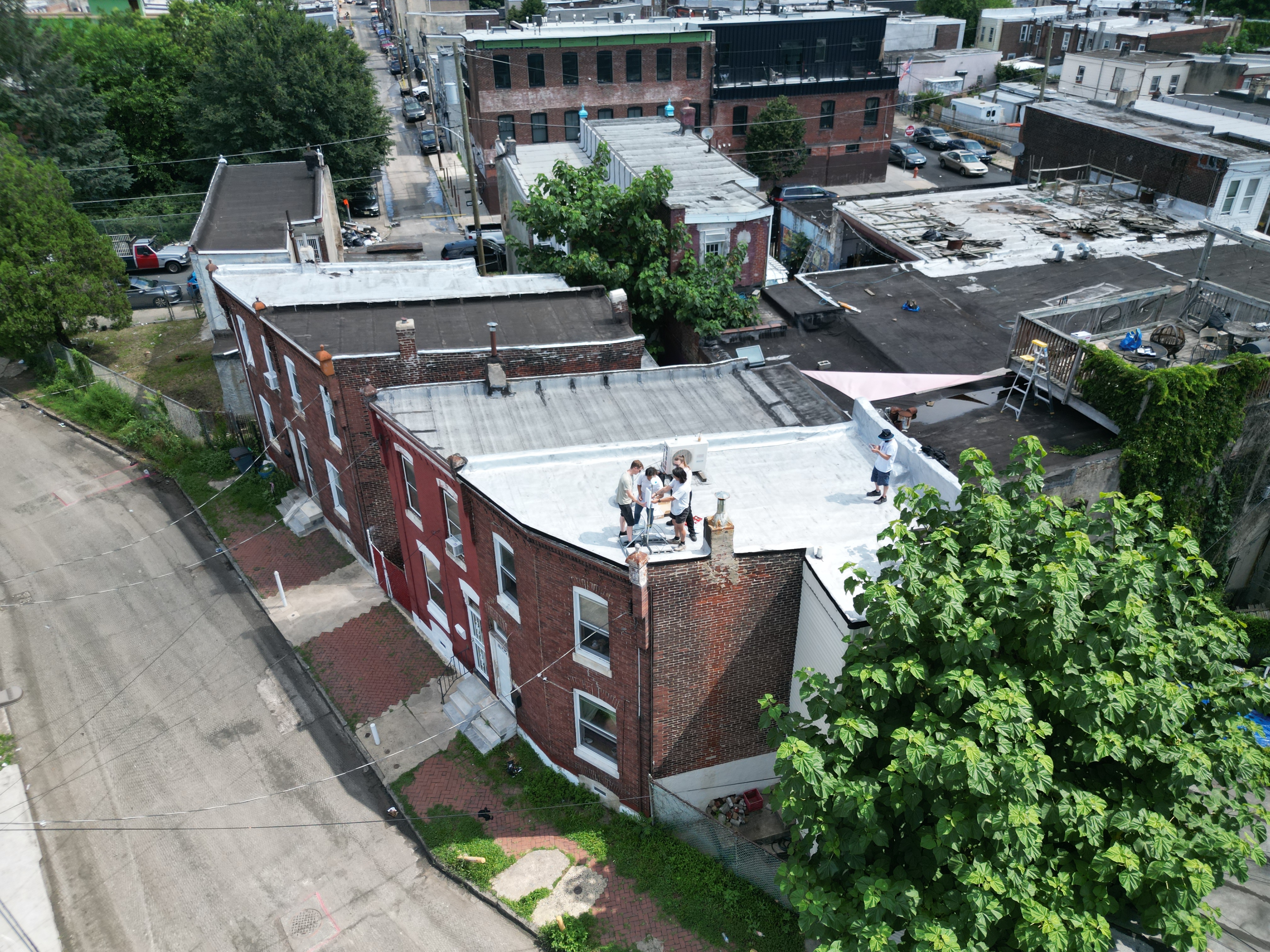 A drone image from above showing 5 people on a rowhome roof, 4 people working on a small structure with an access point device.