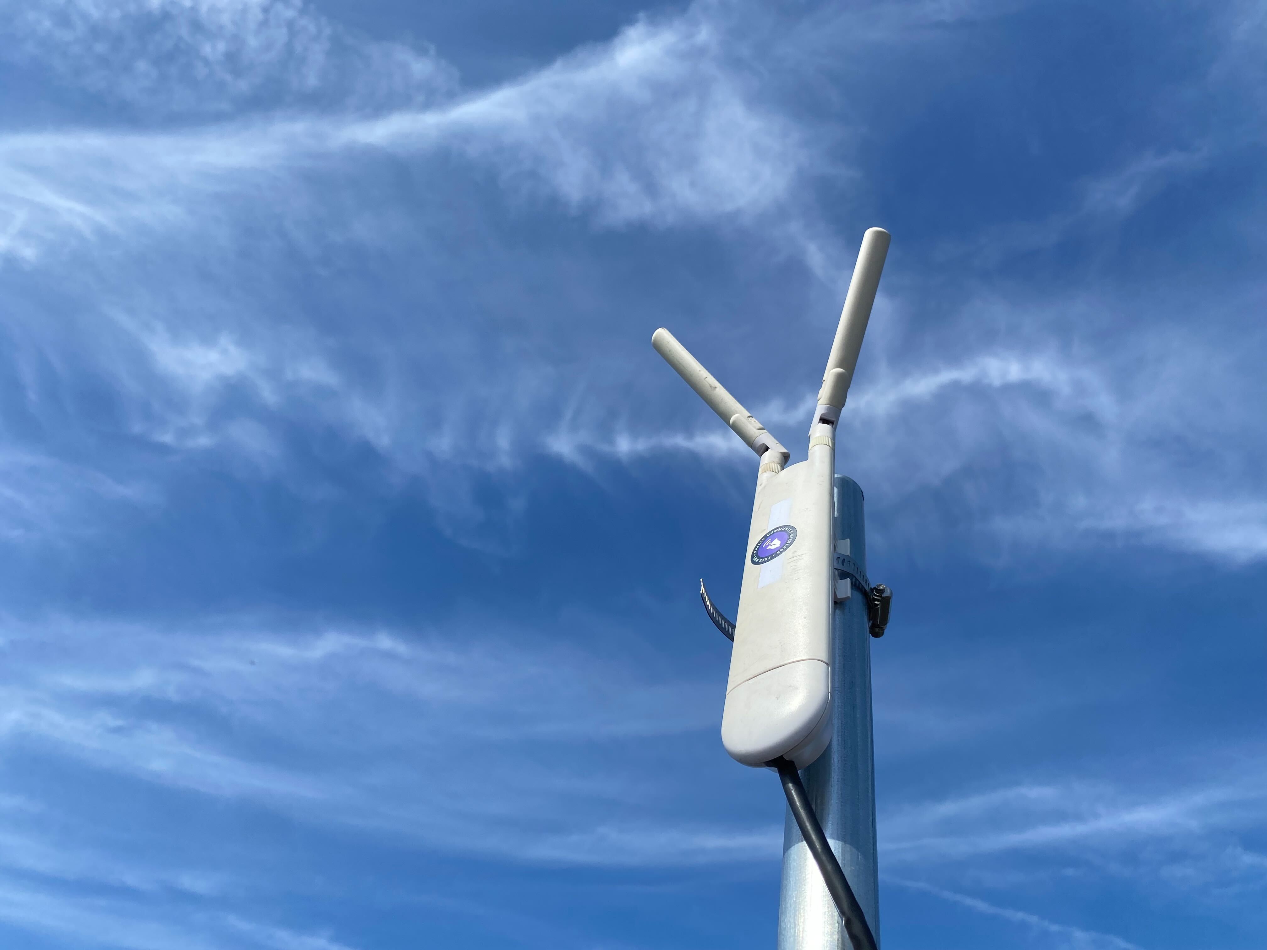 A white access point device on a pole with the sky in the background.