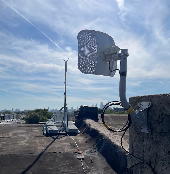 On a roof, a structure with a pole and access point device and a LiteBeam device mounted to a chimney.