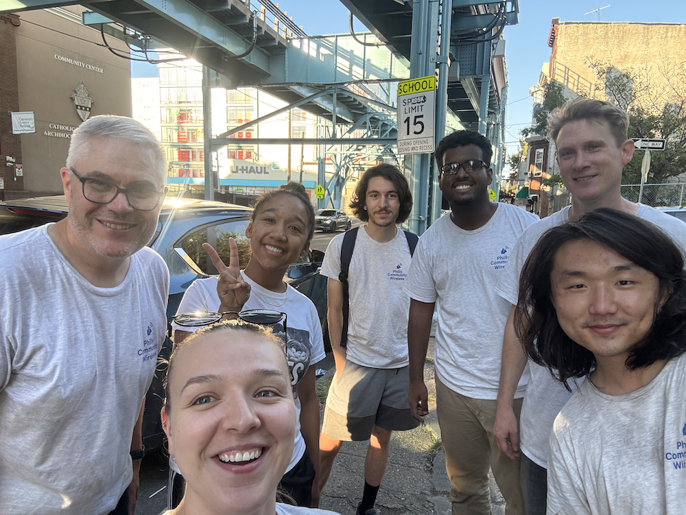7 people in matching PCW t-shirts posing for a photo on a sidewalk.