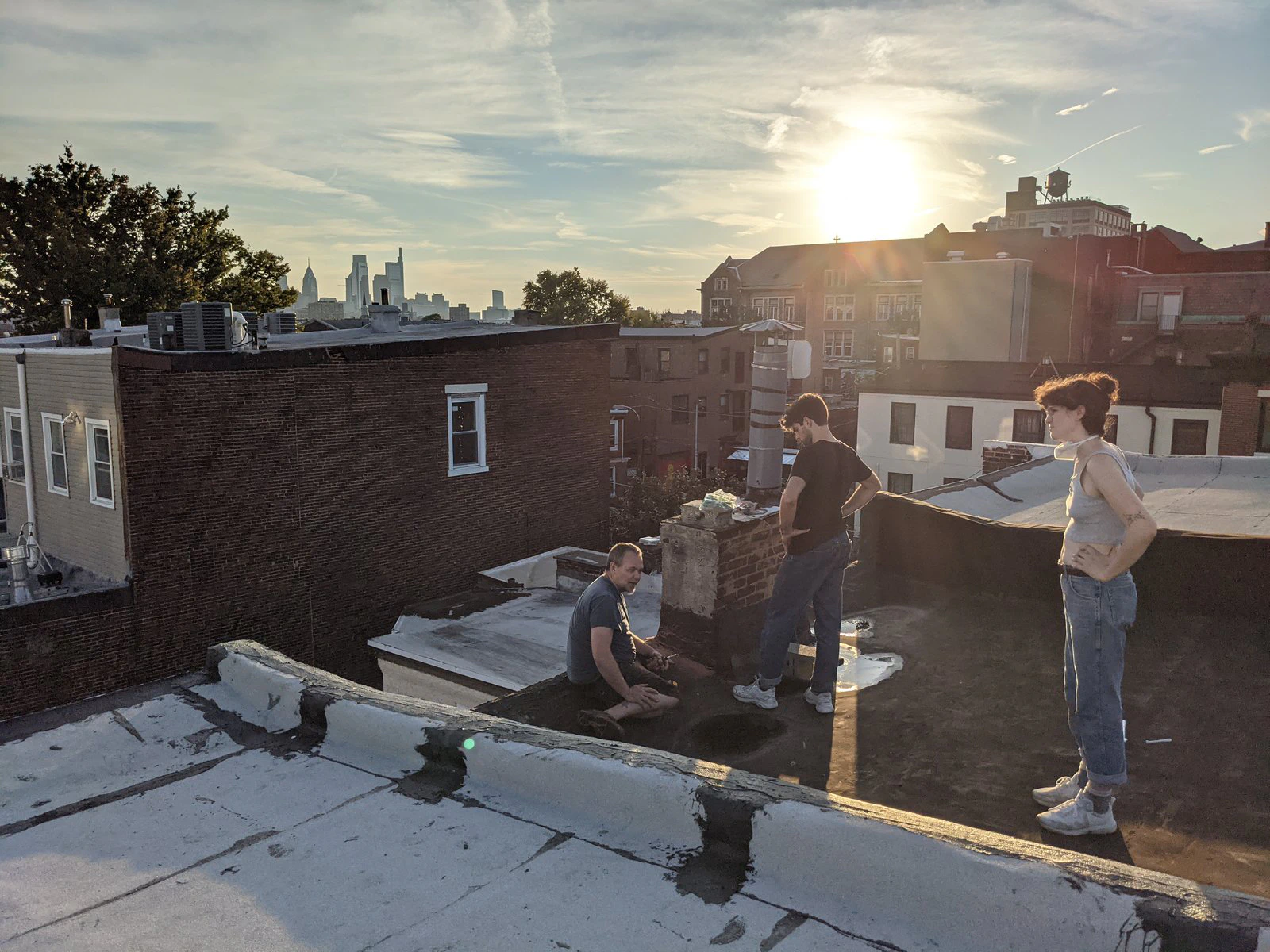 Tres voluntarios en el techo de una casa en hilera al atardecer, con el horizonte de Filadelfia al fondo.