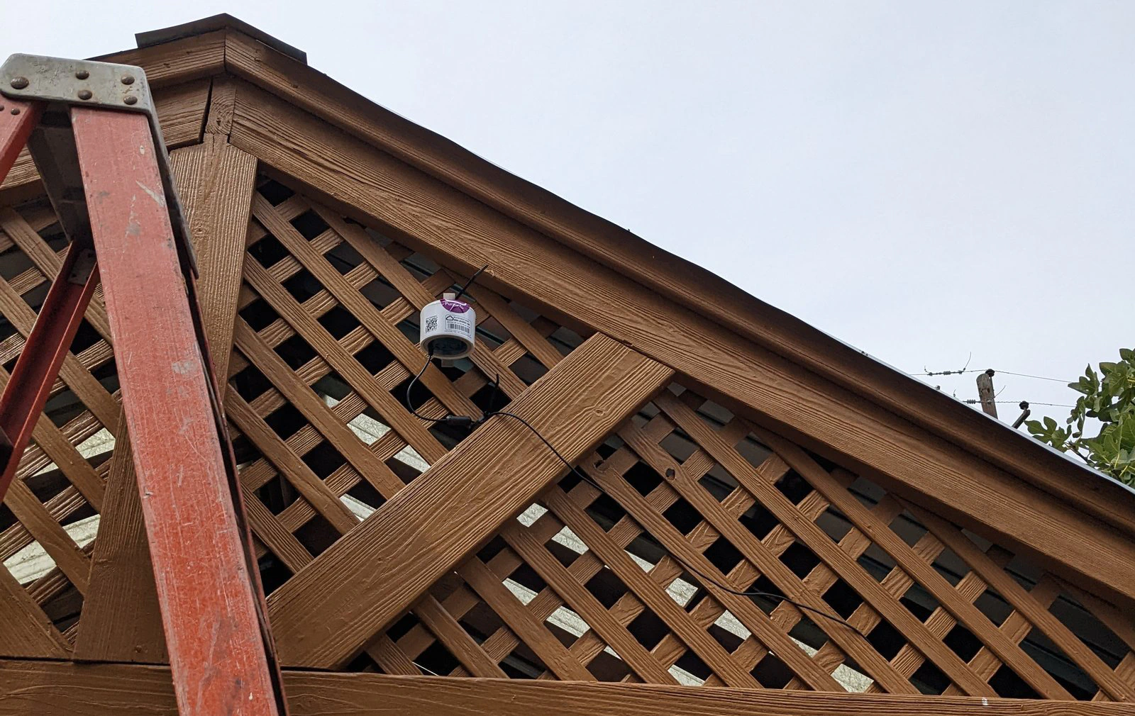 Un monitor PurpleAir instalado en el enrejado de madera de una estructura de jardín.