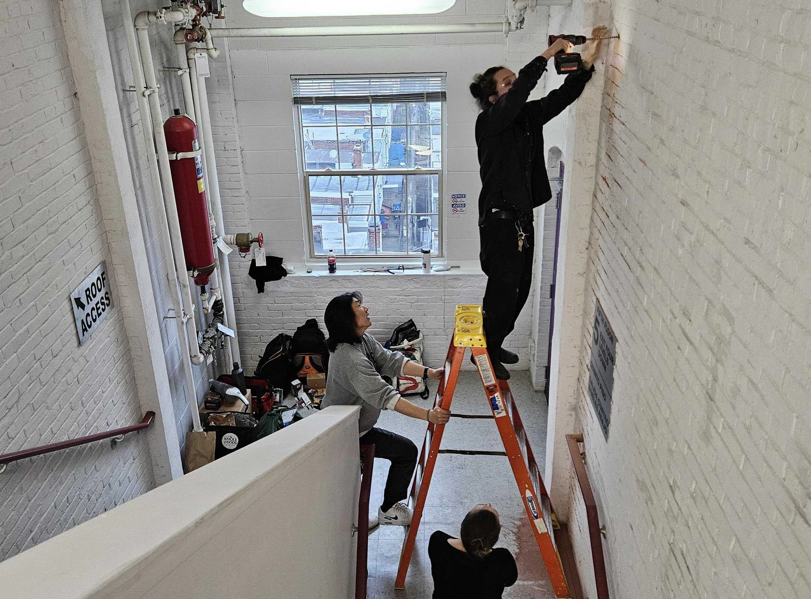 Técnicos sobre una escalera de mano tienden cable a lo largo de la pared de una escalera interior.
