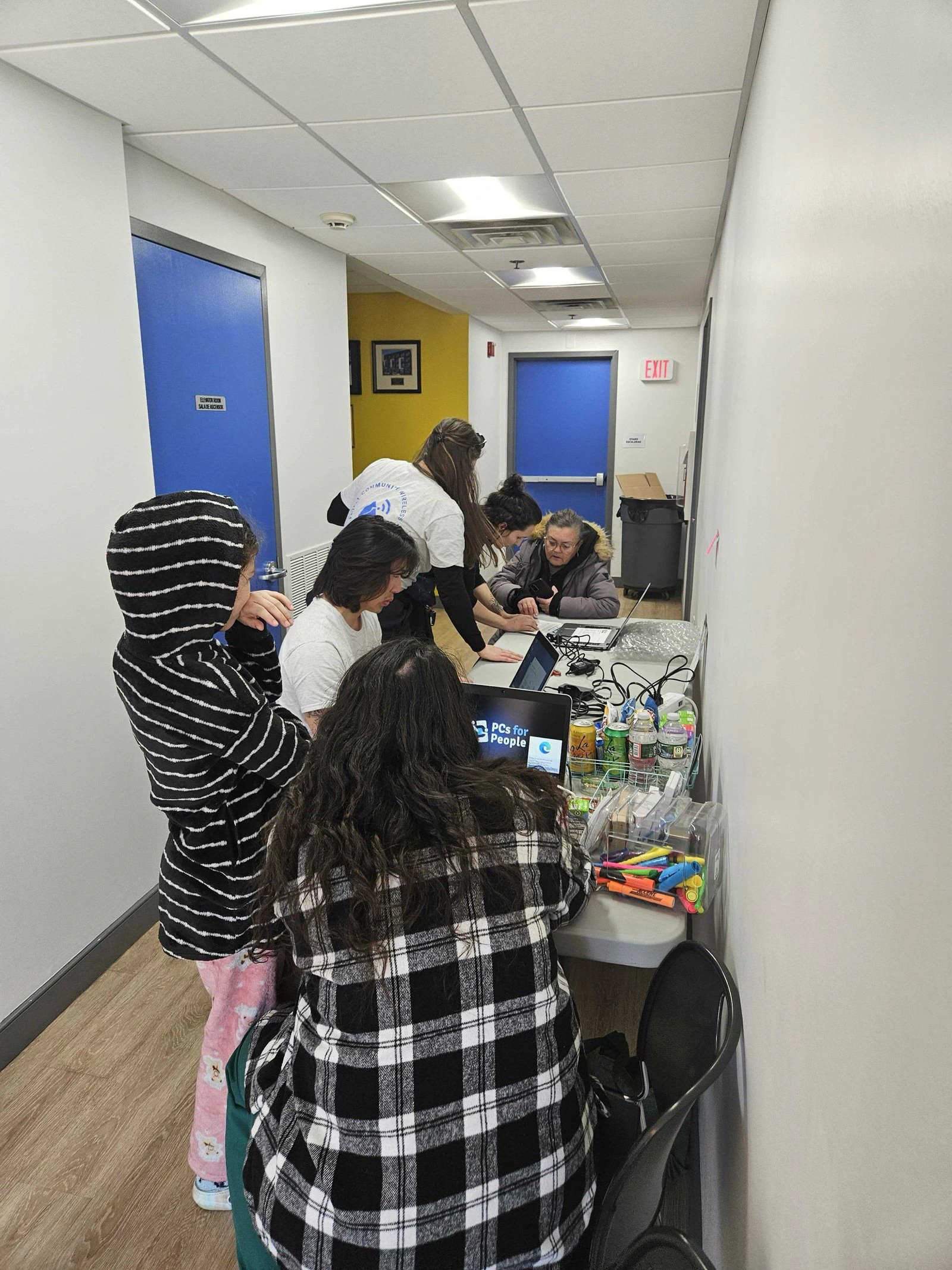 Residentes en una fila de mesas reciben computadoras portátiles en un pasillo.