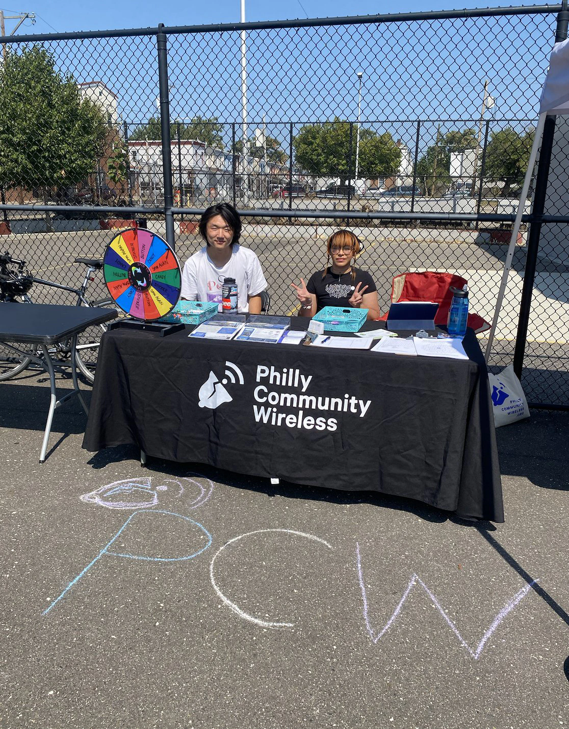 Voluntarios en una mesa de Philly Community Wireless con una ruleta de premios en un parque infantil.