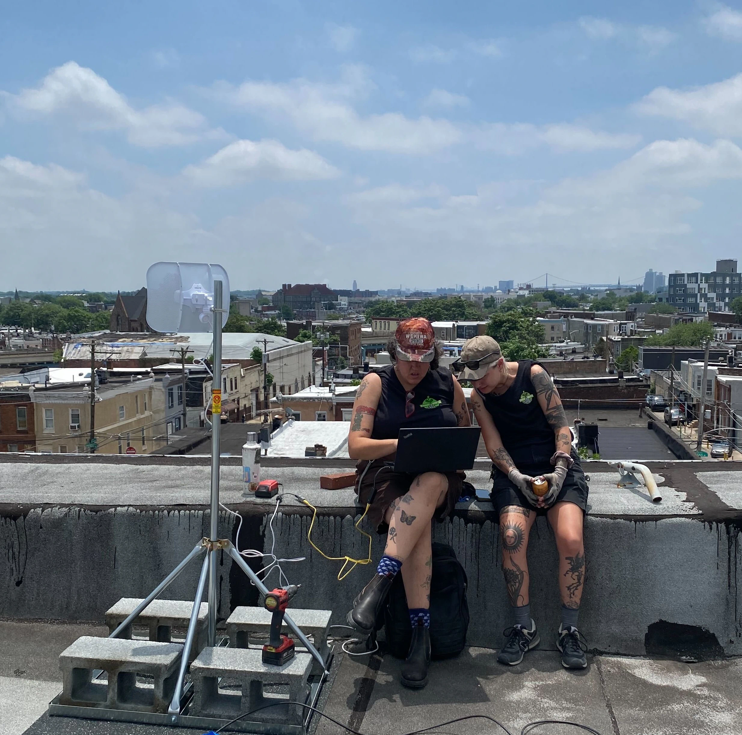 Dos empleados de PhillyWisper sentados en un tejado mirando un ordenador portátil, con una estructura y un dispositivo LiteBeam a su lado.